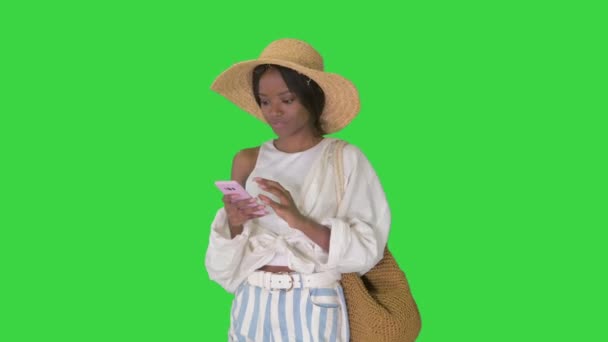 Sonriente joven afroamericana mujer en un sombrero de paja mensajes de texto en su teléfono en una pantalla verde, Chroma Key. — Vídeos de Stock