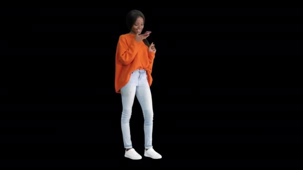 Ładna Afroamerykanka w jasnym swetrze dyktuje wiadomość przez telefon, kanał Alfa. — Wideo stockowe
