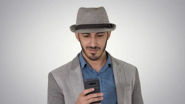 Hombre árabe casual inteligente usando teléfono inteligente mientras camina sobre fondo degradado. —  Fotos de Stock