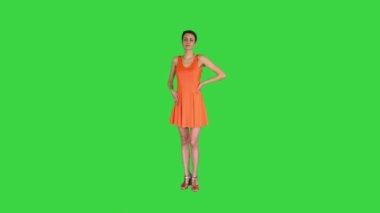 Güzel, neşeli bir kadın yeşil ekranda elbisesini düzeltiyor, Chroma Key.
