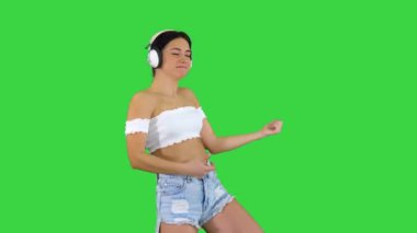 Kafkas kadın model kulaklıklı zıplayarak, mutlu duygularını ifade ederek yeşil ekranda müzik dinliyor, Chroma Key.