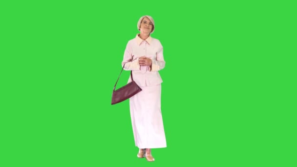 Señora mayor sonriente en gafas y con un bolso caminando sobre una pantalla verde, Chroma Key. — Vídeo de stock