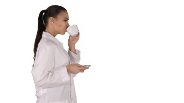 Genç hemşire beyaz arka planda yürürken kahve ya da çay içerek rahatlıyor..