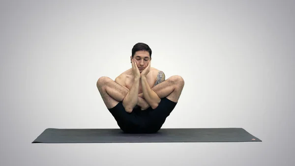 Musculoso joven guapo haciendo ejercicio, yoga, loto, manos en la cara sobre fondo degradado. —  Fotos de Stock