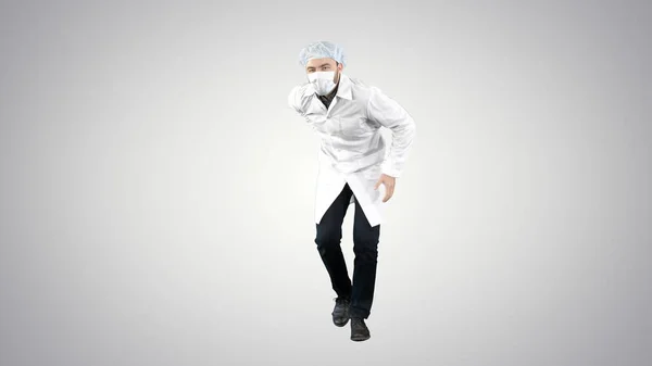 Dokter draagt zijn uniform en draagt een masker hij loopt op een grappige manier op een gradiënt achtergrond. — Stockfoto