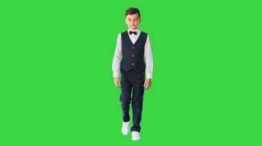 Yelekli ve papyonlu küçük bir çocuk Yeşil Ekran 'a doğru yürüyor, Chroma Key.