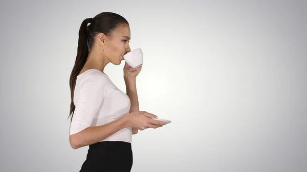 Hermosa mujer morena con taza blanca con té o café caminando sobre fondo degradado. — Foto de Stock