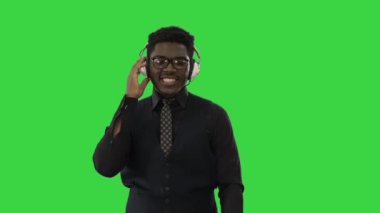 Gülümseyen Afro-Amerikan kulaklıklı adam yeşil ekranda yürürken ve kameraya bakarken müzik dinliyor, Chroma Key.