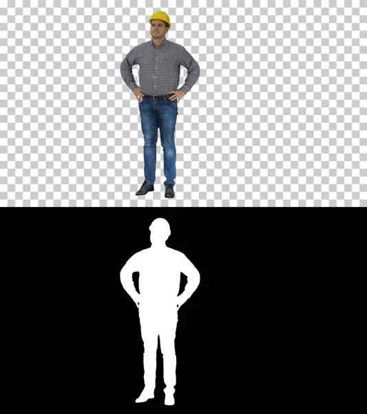 Leende byggarbetare i gul hjälm tittar på perfekt välbyggt objekt händer på höfter, Alpha Channel — Stockfoto