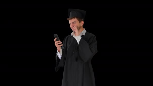 Lachender männlicher Student in Abschlussanzug und Mörtelbrett mit Videoanruf auf seinem Telefon, Alpha Channel — Stockvideo