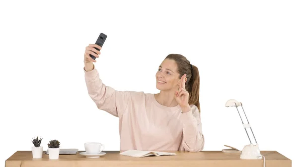 Schöne Frau macht ein Selfie mit ihrem Handy am Schreibtisch auf weißem Hintergrund. — Stockfoto