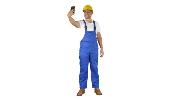 Souriant beau jeune constructeur faisant selfie avec téléphone mobile sur fond blanc. — Photo