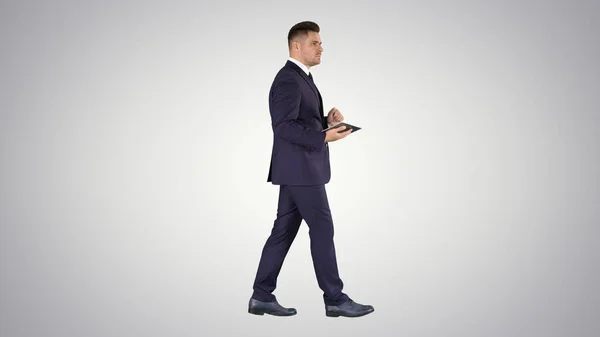 Elegante joven hombre de negocios utilizando su tableta de PC mientras camina sobre fondo degradado. — Foto de Stock
