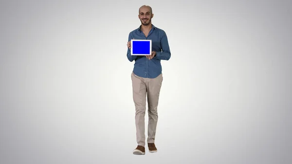 Homem árabe andando e mostrando tablet apresentando algo no fundo gradiente. — Fotografia de Stock