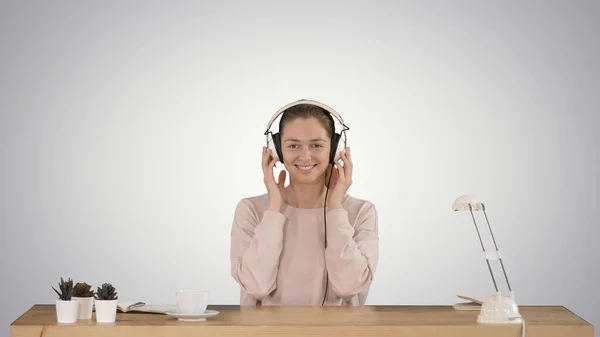 Jovem mulher sorrindo colocando fones de ouvido e ouvindo música no fundo gradiente. — Fotografia de Stock