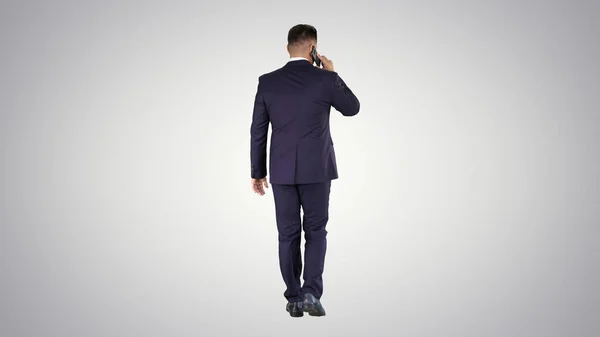 Caminar hombre de negocios con hablar en el teléfono móvil en el fondo gradiente. —  Fotos de Stock