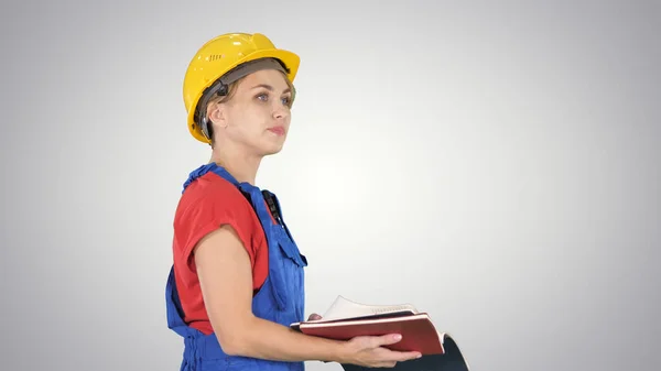 Mujer trabajadora de la construcción en sombrero duro y uniforme de ropa de trabajo comprobando la lista en el fondo del gradiente. —  Fotos de Stock