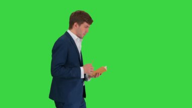 Düşünen iş adamı yeşil ekranda yürürken defterine notlar yazıyor, Chroma Key.