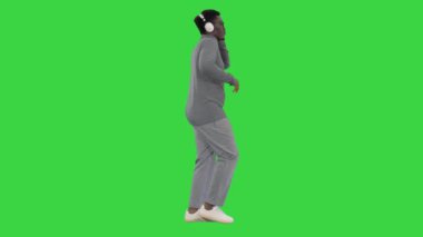 Gülümseyen Afrikalı Amerikalı bir adam tek eliyle kulaklık tutuyor ve yeşil ekranda yürürken müzik dinliyor, Chroma Key.
