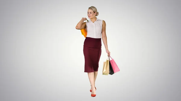 Mulher feliz segurando sacos de compras, sorrindo e andando em fundo gradiente. — Fotografia de Stock