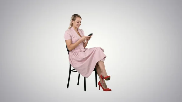 Mujer reflexiva en vestido rosa mensajes de texto en el teléfono inteligente sobre fondo degradado. —  Fotos de Stock