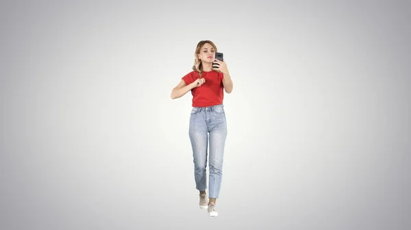 Bionda che cammina e si pavoneggia guardando al telefono su sfondo sfumato. — Foto Stock