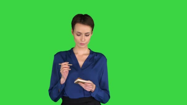 Задумчивая молодая женщина в элегантной повседневной одежде трогает губу карандашом и ищет идею и записывает ее на зеленый экран, хрома ключ. — стоковое видео