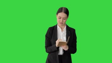 Takım elbiseli konsantre bir kadın yeşil ekranda yürürken not defterine iş fikirleri yazıyor, Chroma Key.