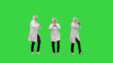 Beyaz cüppeli ve koruyucu şapkalı üç erkek doktor eş zamanlı dans edip yeşil ekran Chroma Key 'deki kameraya bakıyor..