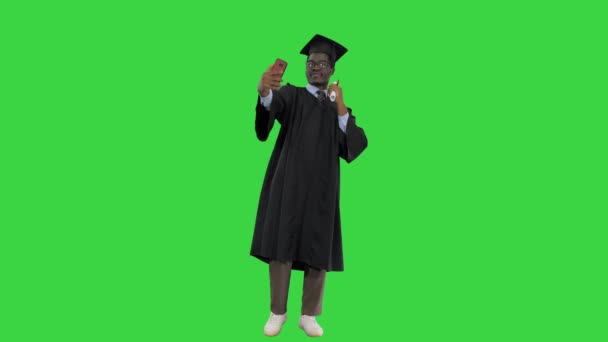 Glücklicher afrikanisch-amerikanischer Student im Abschlussgewand, der auf einem Green Screen, Chroma Key, Telefon-Selfies mit seinem Diplom macht. — Stockvideo