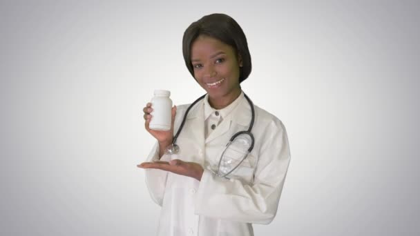 Smiling african american female doctor with stethoscope advertising medicine on gradient background. — Stock Video