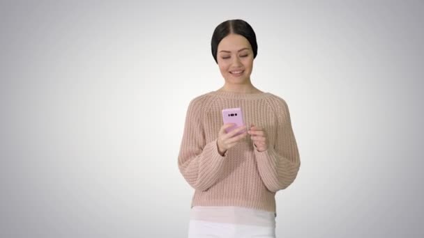 Pěkná mladá žena textové zprávy na mobilním telefonu při chůzi na gradient pozadí. — Stock video