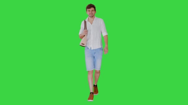 Schöner lächelnder Mann im weißen Hemd, der mit einer Tasche auf der Schulter auf einem Green Screen wandelt, Chroma Key. — Stockvideo