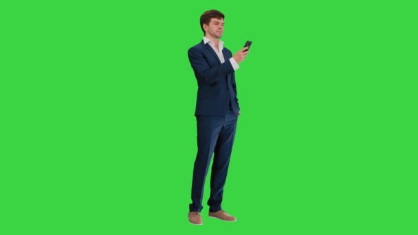 Seriöser Geschäftsmann schaut auf sein Telefon auf einem grünen Bildschirm, Chroma Key. — Stockvideo