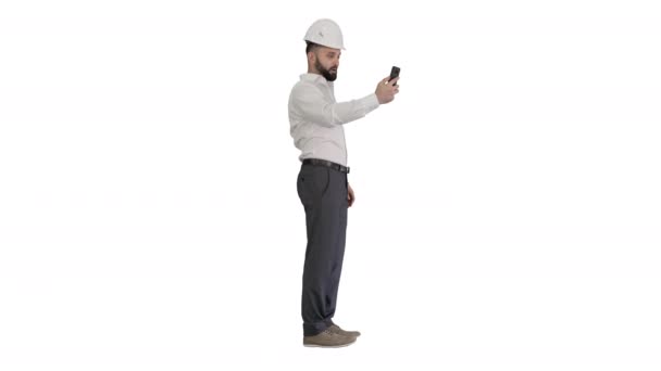 Homme ingénieur portant casque de sécurité et chemise de protection faire appel vidéo sur fond blanc. — Video