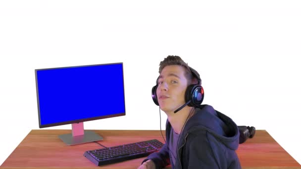 Gamer parler à la caméra assis à côté de PC Monitor sur fond blanc. — Video