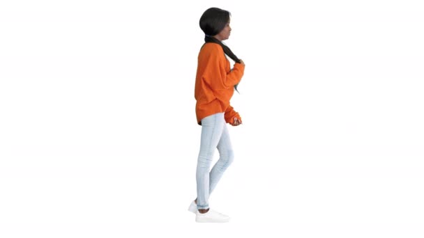 Улыбающаяся афроамериканка в ярком свитере и джинсах позирует руками в карманах на белом фоне. — стоковое видео