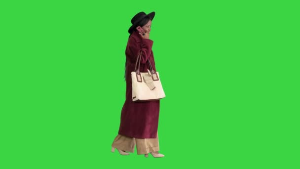 Afrykański amerykański moda dziewczyna w płaszcz i czarny kapelusz mówi przez telefon podczas chodzenia na zielonym ekranie, Chroma Key. — Wideo stockowe
