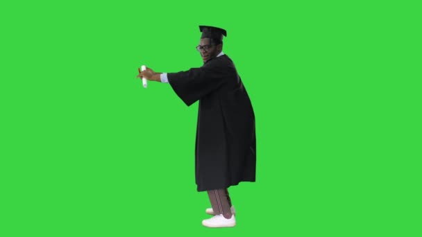 Aufgeregter afrikanisch-amerikanischer Student in Abschlussrobe tanzt glücklich mit seinem Diplom auf einem Green Screen, Chroma Key. — Stockvideo