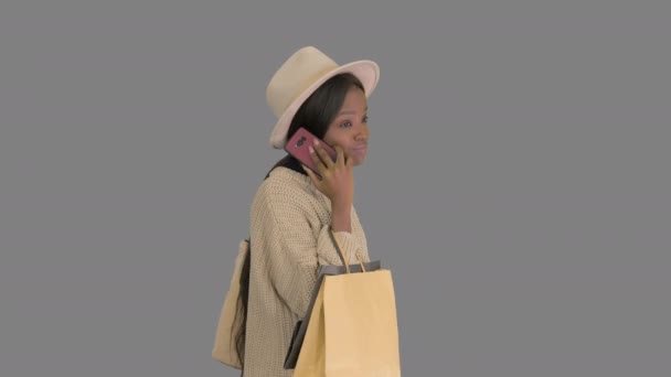 Büyük beden örgü ve şapkalı Afrikalı kız alışveriş torbalarıyla yürürken telefonla konuşuyor, Alpha Channel. — Stok video