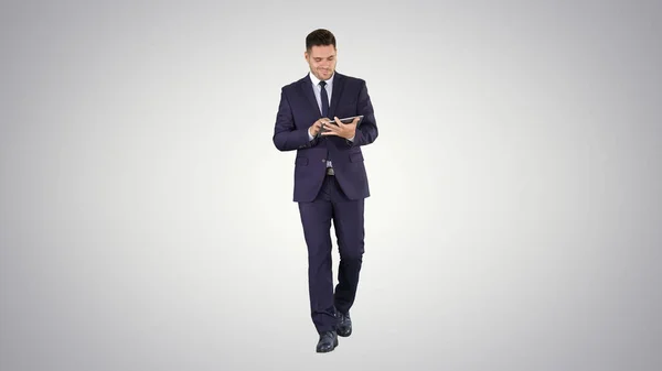 Mężczyzna w garniturze chodzenia i korzystania z tabletu cyfrowego na gradientowym backgro — Zdjęcie stockowe