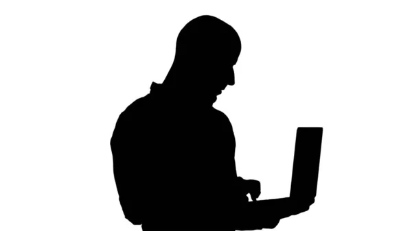 Silhouette Junger Geschäftsmann aus dem Nahen Osten steht und tippt auf seinem Laptop, wenn er ihn in der Hand hält. — Stockfoto