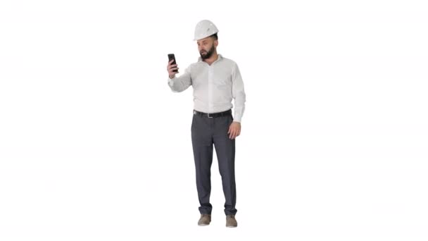 Homme ingénieur portant casque de sécurité et chemise de protection faire appel vidéo sur fond blanc. — Video