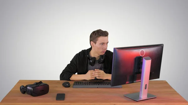 Serious gamer sitting at computer watching a game on gradient ba — Stock Photo, Image