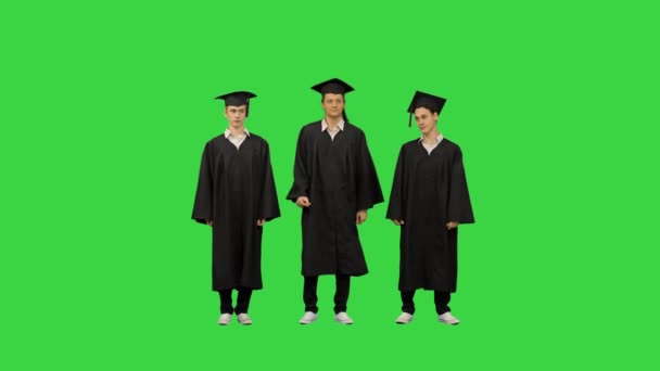 Drei männliche Studenten in Abschlussroben und Mörtelbrettern wärmen sich auf, während sie auf einem Green Screen warten, Chroma Key. — Stockvideo