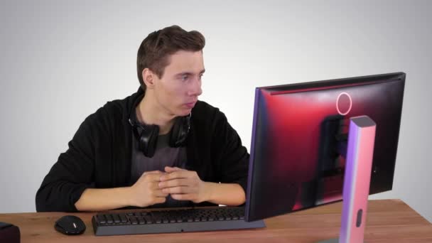 Joueur sérieux assis à l'ordinateur regardant un jeu sur fond de dégradé. — Video