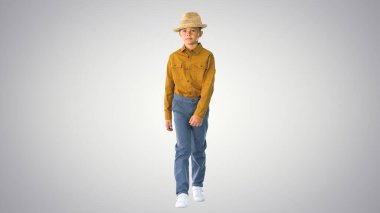 Hasır şapkasını düzelten tişörtlü çocuk yürürken ve ararken