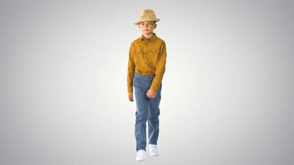 Мальчик в рубашке регулирует свою соломенную шляпу во время ходьбы и глядя — стоковое фото