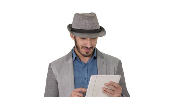 Guapo sonriente árabe hombre en un sombrero caminando y usando tableta sobre fondo blanco. —  Fotos de Stock