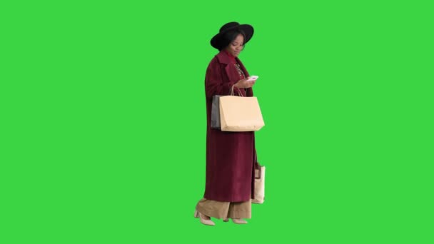 Sorridente afroamericana ragazza di moda in cappotto e cappello nero sms sul suo telefono su uno schermo verde, Chroma Key. — Video Stock